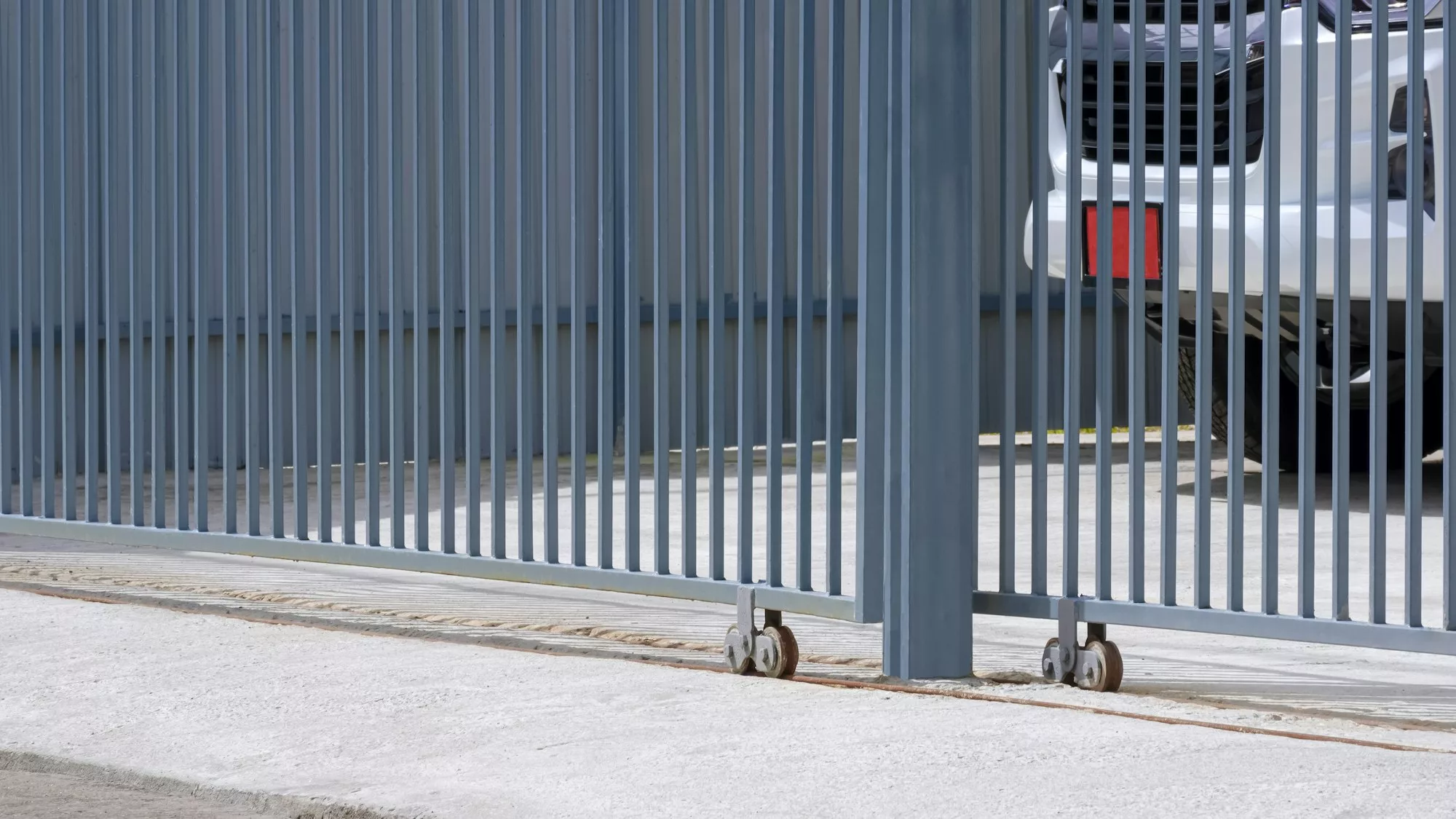 Side view of sliding metal fence gate in front of house with a car parking inside of area